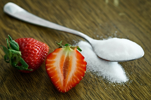 Lyžička cukru a rozrezaní jahoda 